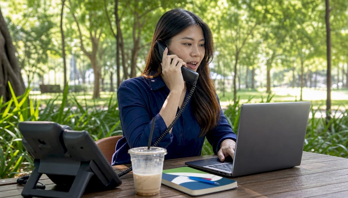 Person using a VoIP phone and laptop while working remotely
